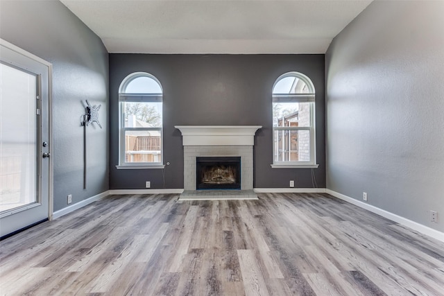 unfurnished living room with wood finished floors, a fireplace, baseboards, and a textured wall