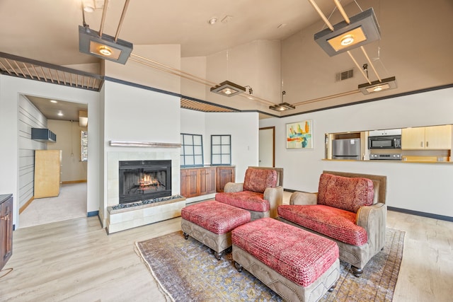 living area with light wood finished floors, visible vents, a tiled fireplace, and high vaulted ceiling