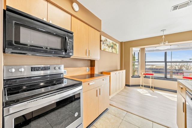 kitchen featuring light brown cabinetry, stainless steel electric range, black microwave, and a healthy amount of sunlight
