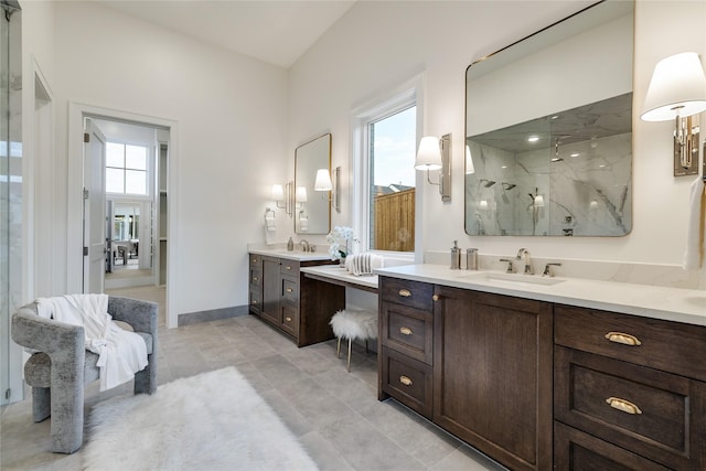 full bath with a marble finish shower, two vanities, baseboards, and a sink