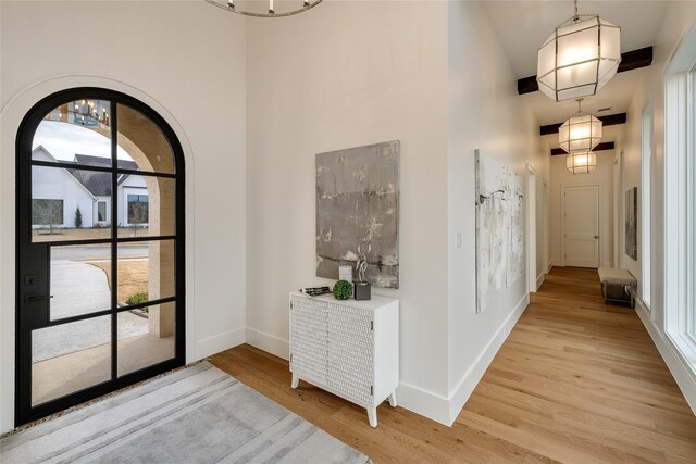 hallway featuring a chandelier, baseboards, light wood-style floors, and a towering ceiling