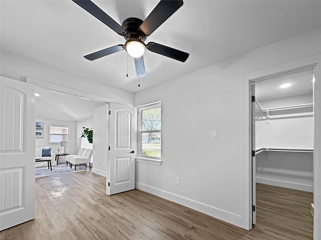 bedroom with a walk in closet, baseboards, light wood finished floors, ceiling fan, and a closet