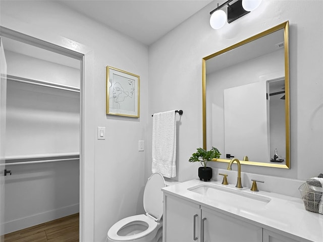 bathroom featuring toilet, a walk in closet, wood finished floors, and vanity