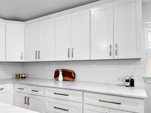 kitchen with white cabinets, decorative backsplash, and light stone counters