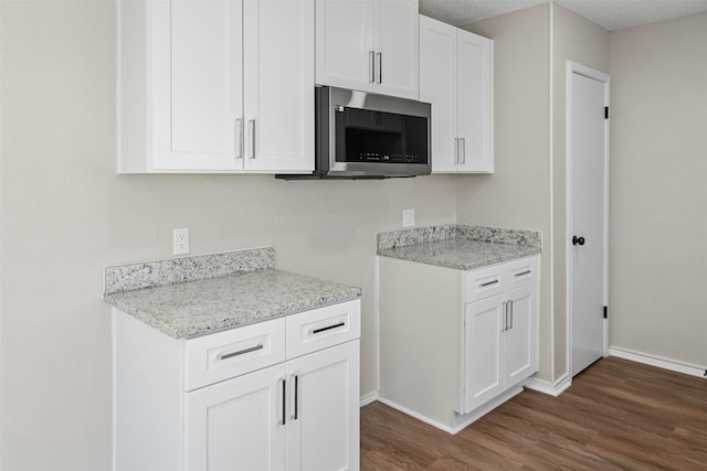 1505 W Collin, Corsicana, TX 75110 - kitchen with stainless steel microwave, dark wood-style floors, baseboards, white cabinets, and light stone counters