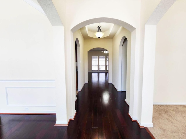 hall with baseboards, dark wood-style flooring, and a tray ceiling
