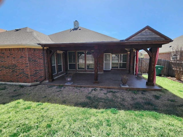 back of house featuring fence, a lawn, a shingled roof, and brick siding