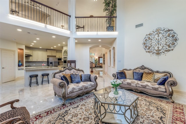12252 Skipper Dr, Frisco, TX 75035 - living room featuring arched walkways, light marble finish flooring, a high ceiling, recessed lighting, and baseboards