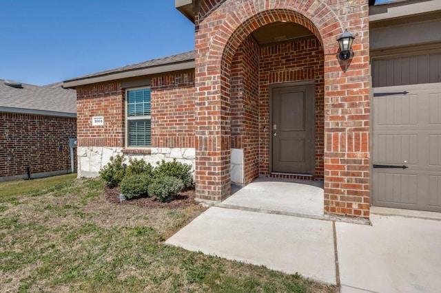 doorway to property featuring an attached garage, brick siding, and a shingled roof