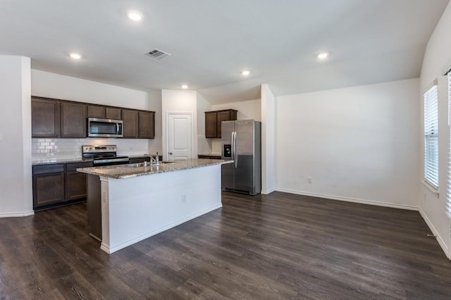 kitchen featuring visible vents, a kitchen island with sink, backsplash, stainless steel appliances, and dark brown cabinetry