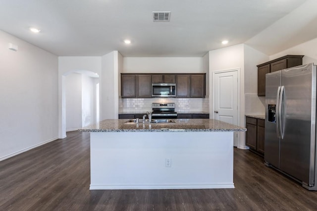 kitchen with visible vents, an island with sink, arched walkways, stainless steel appliances, and dark wood-type flooring