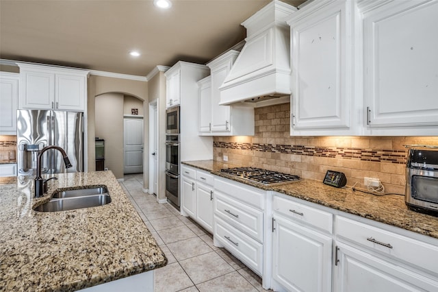 9848 Robinwoods Dr, Frisco, TX 75035 - kitchen with appliances with stainless steel finishes, arched walkways, custom exhaust hood, a sink, and white cabinetry