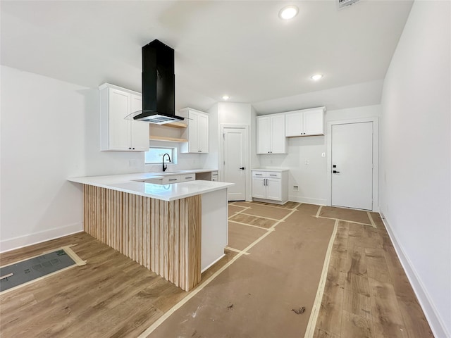 kitchen featuring ventilation hood, baseboards, light wood finished floors, a peninsula, and a sink