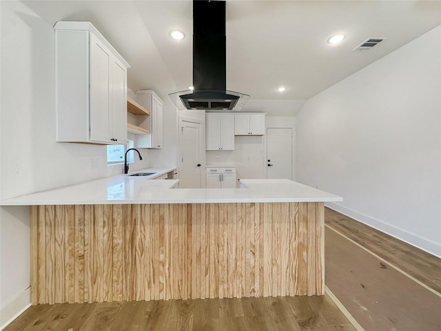 kitchen with visible vents, open shelves, a peninsula, island exhaust hood, and a sink