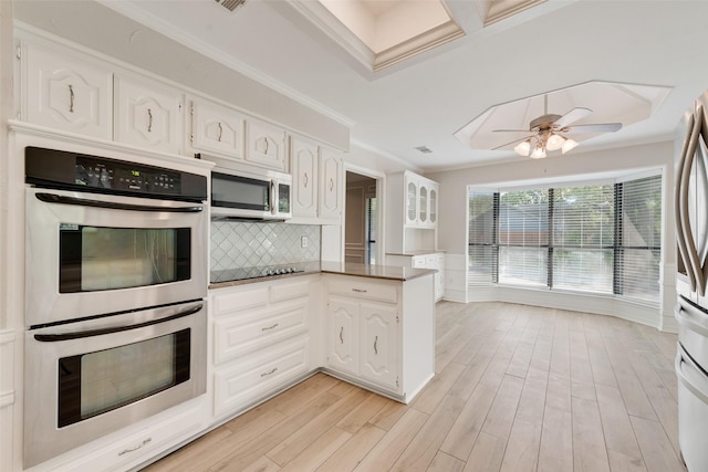 kitchen featuring crown molding, decorative backsplash, a peninsula, white cabinetry, and appliances with stainless steel finishes