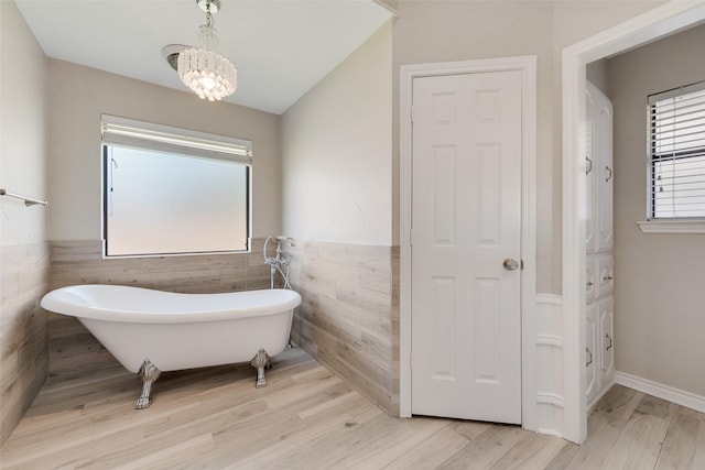 bathroom featuring a wainscoted wall, a freestanding tub, wood finished floors, and tile walls