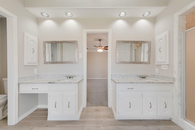 bathroom featuring a sink, a ceiling fan, wood finished floors, and two vanities