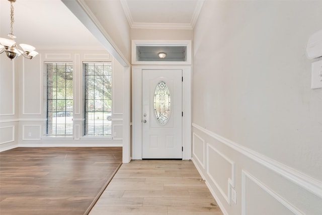 foyer entrance with an inviting chandelier, ornamental molding, light wood-style flooring, and a decorative wall