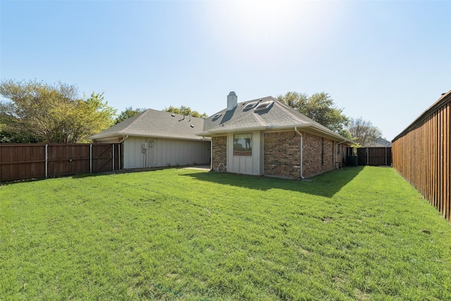 back of house featuring a fenced backyard, a chimney, a lawn, and brick siding