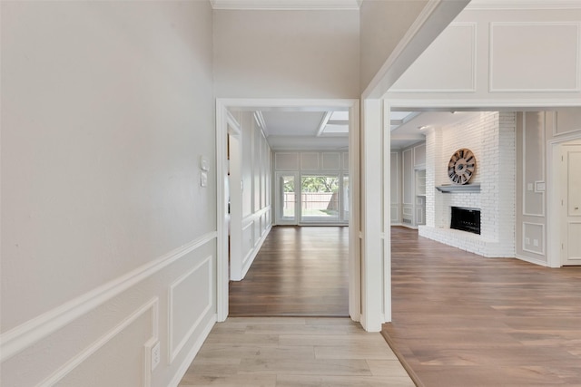 corridor with a wainscoted wall, ornamental molding, a decorative wall, and light wood-style flooring