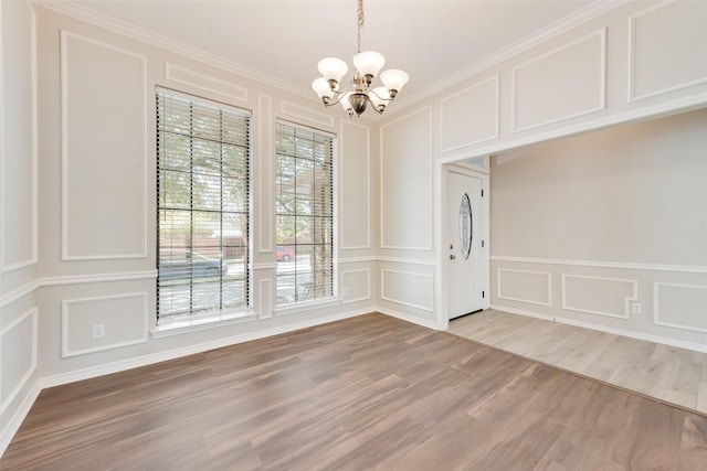 unfurnished dining area with light wood-type flooring, ornamental molding, a decorative wall, and a notable chandelier