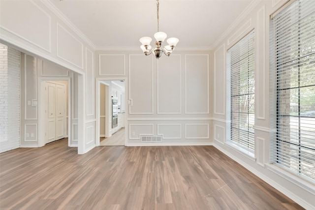 unfurnished dining area featuring a notable chandelier, light wood-style flooring, visible vents, and a decorative wall