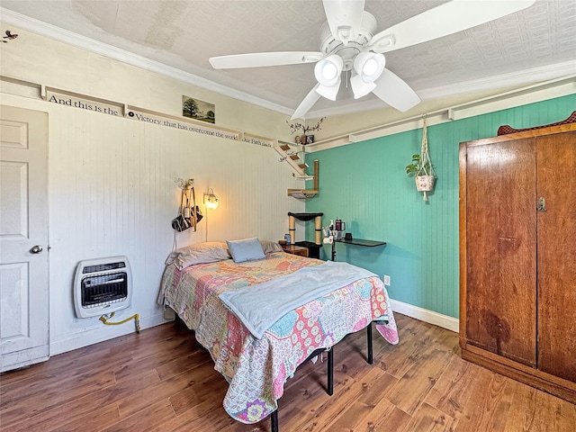 bedroom featuring baseboards, ornamental molding, wood finished floors, a ceiling fan, and heating unit
