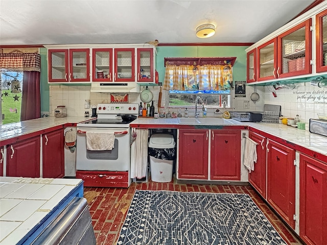 kitchen with light countertops, a sink, white electric range oven, under cabinet range hood, and decorative backsplash