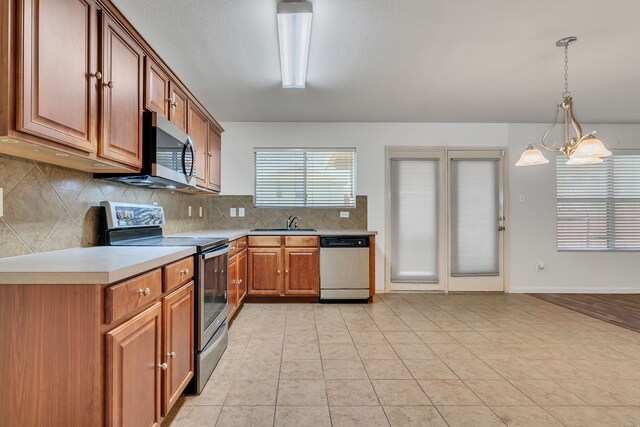 8529 Star Thistle Dr, Fort Worth, TX 76179 - kitchen featuring brown cabinets, backsplash, stainless steel appliances, light countertops, and hanging light fixtures
