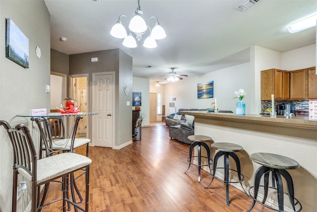 1017 Story Book Ln, Weatherford, TX 76086 - kitchen featuring light wood finished floors, a breakfast bar, visible vents, brown cabinetry, and ceiling fan with notable chandelier