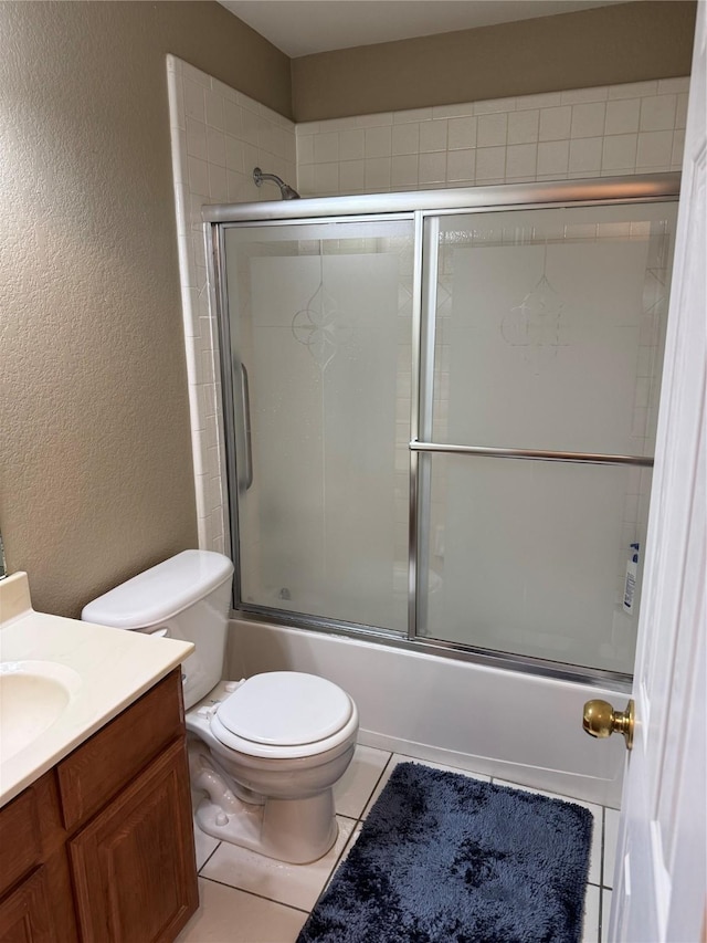 bathroom featuring vanity, shower / bath combination with glass door, tile patterned flooring, toilet, and a textured wall