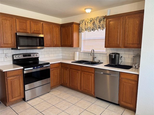 kitchen with a sink, backsplash, appliances with stainless steel finishes, brown cabinetry, and light countertops