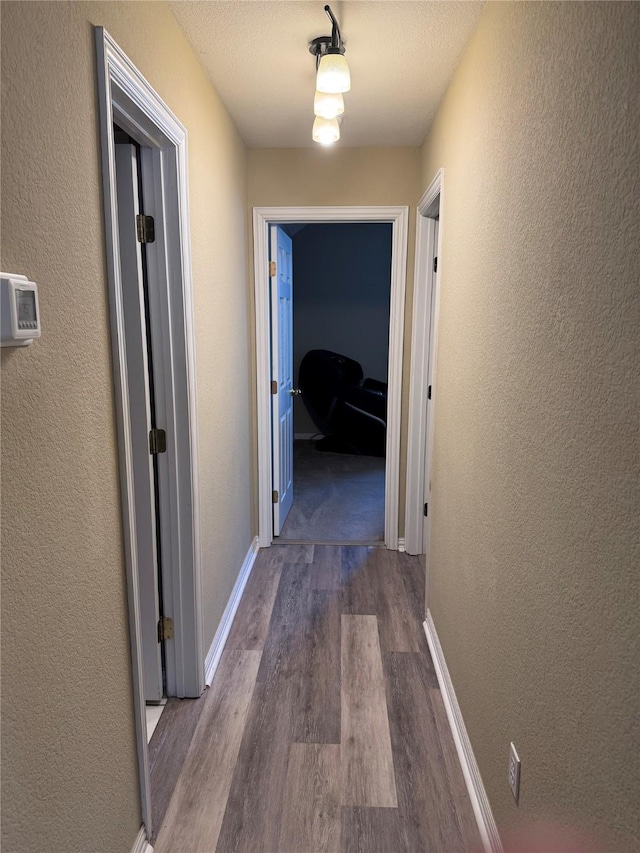 hall with a textured wall, baseboards, and dark wood-style flooring