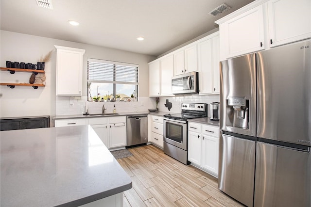 2015 Brenham Dr, Forney, TX 75126 - kitchen featuring appliances with stainless steel finishes, a sink, white cabinetry, decorative backsplash, and light wood finished floors