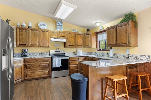 251 Dunn Dr, Palo Pinto, TX 76484 - kitchen featuring appliances with stainless steel finishes, under cabinet range hood, vaulted ceiling, a peninsula, and brown cabinets