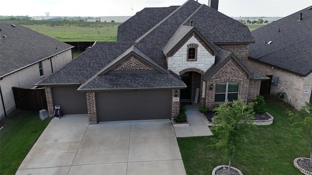 french country style house featuring a shingled roof, brick siding, a garage, a front yard, and concrete driveway