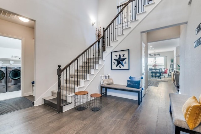 stairway with a towering ceiling, wood finished floors, and washer and clothes dryer