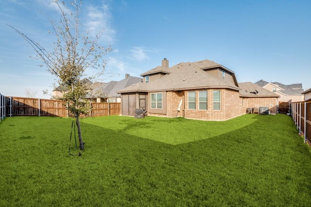 rear view of property with a lawn, a fenced backyard, a chimney, and brick siding