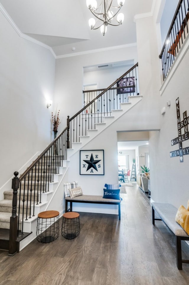 staircase with ornamental molding, wood finished floors, and a notable chandelier