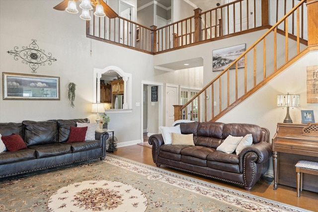 living room featuring a ceiling fan, baseboards, a towering ceiling, wood finished floors, and stairway