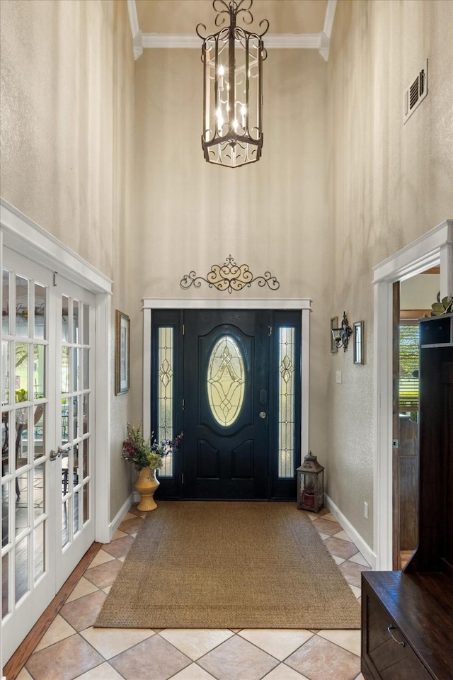 foyer entrance featuring tile patterned flooring, ornamental molding, visible vents, and a towering ceiling