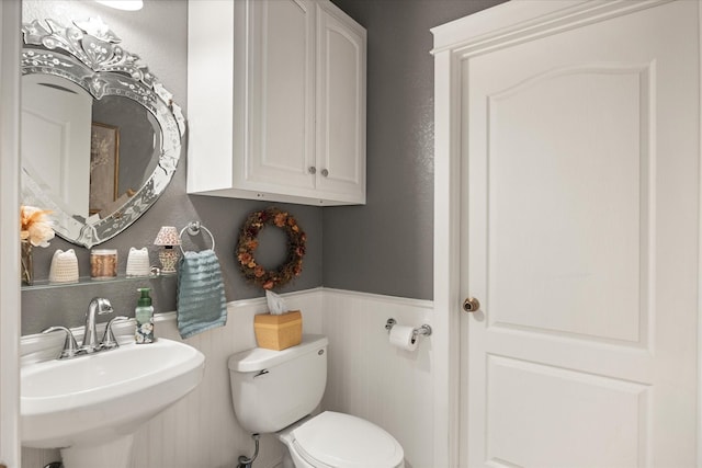 half bath with toilet, wainscoting, and a sink