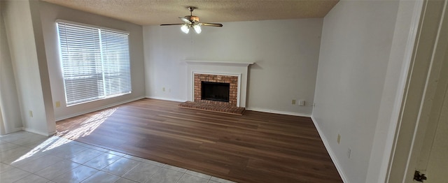 unfurnished living room featuring tile patterned flooring, baseboards, ceiling fan, a fireplace, and a textured ceiling