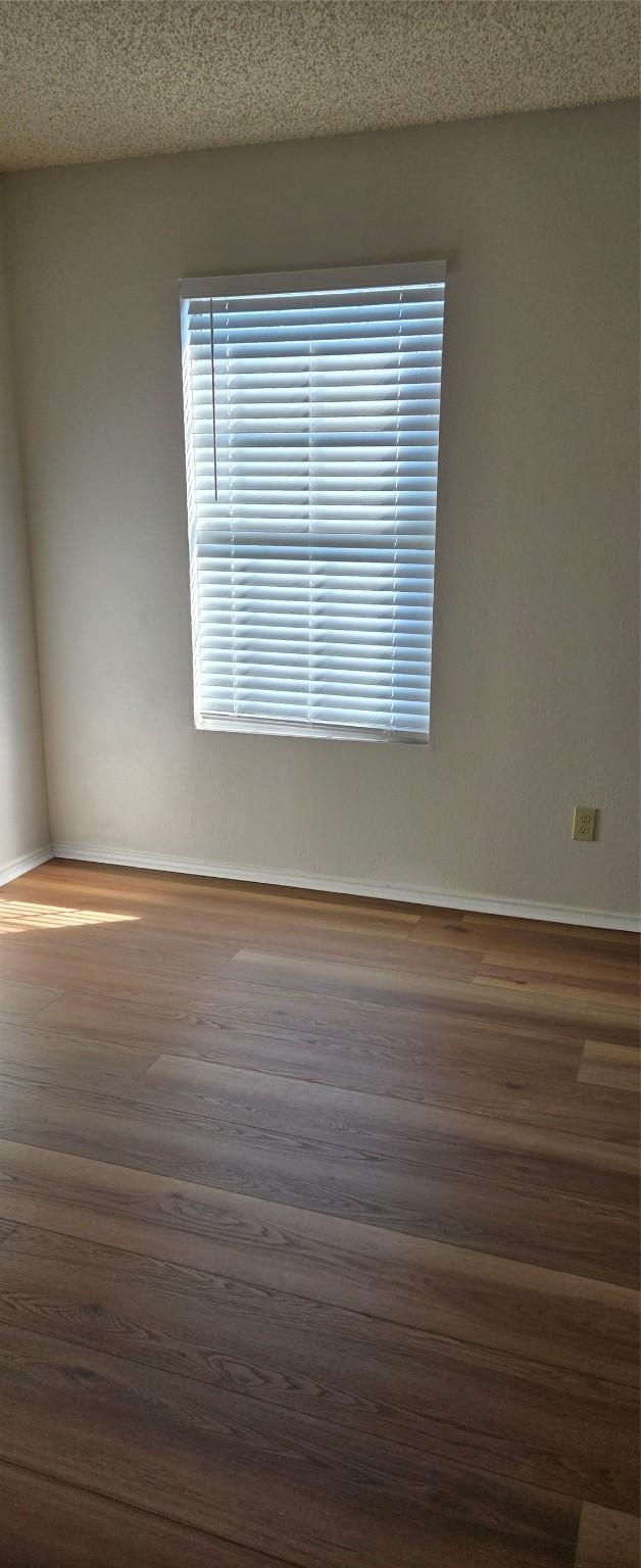 spare room with a textured ceiling, baseboards, and wood finished floors