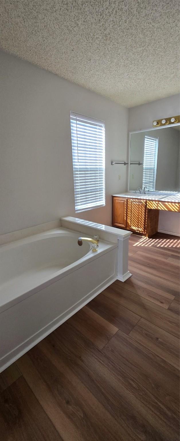 full bath featuring vanity, a garden tub, a healthy amount of sunlight, and a textured ceiling