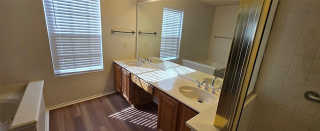 bathroom featuring a sink, wood finished floors, double vanity, baseboards, and a bath