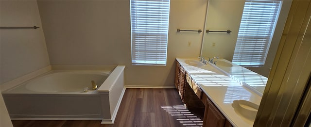 full bath with a bath, vanity, baseboards, and wood finished floors