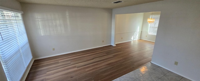 unfurnished room featuring dark wood finished floors, baseboards, visible vents, and a textured ceiling