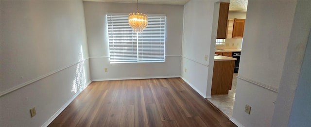 unfurnished dining area featuring baseboards, an inviting chandelier, and wood finished floors