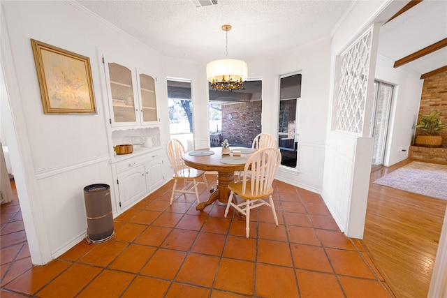 4379 Capra Way, Benbrook, TX 76126 - dining room with a chandelier, crown molding, a textured ceiling, a decorative wall, and dark tile patterned flooring